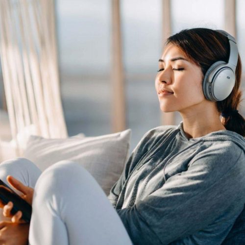 A girl is listening to mimi enabled headphones on sofa